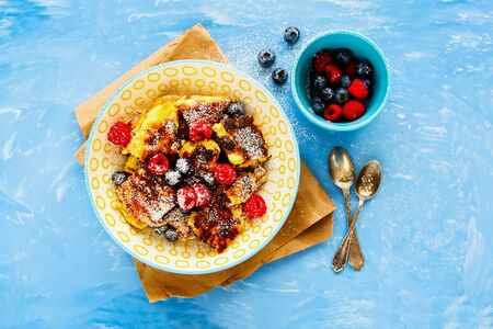 Flat-lay of shredded pancake with fresh berries on blue board from above の写真素材