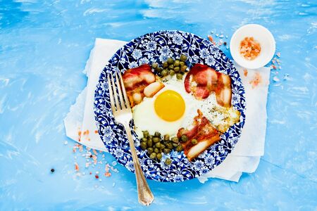 English breakfast with fried egg and bacon on blue background flat layの写真素材