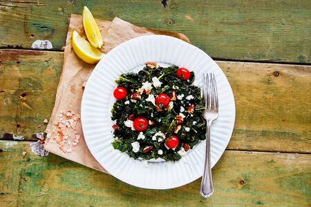 Salad with kale, feta, nuts and tomato on wooden background flat layの写真素材