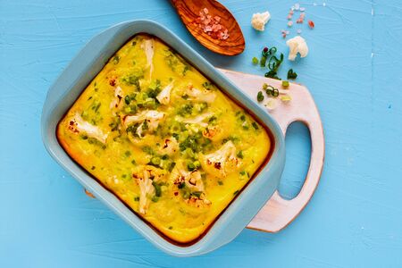Flat-lay of Cauliflower Gratin in baking dish on blue board from aboveの写真素材