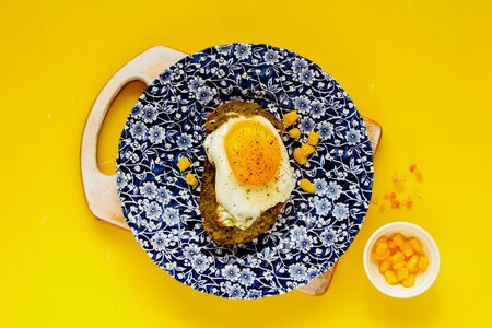 Flat-lay of fried egg sandwich with sweet corn and pesto sauce on yellow boardの写真素材