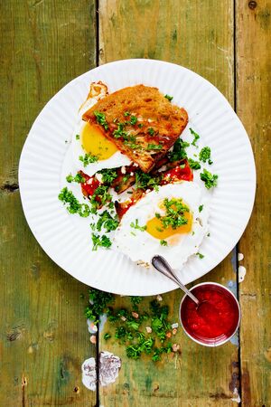 Flat-lay of fried eggs with fresh herbs  on grilled bread over old wooden tableの写真素材