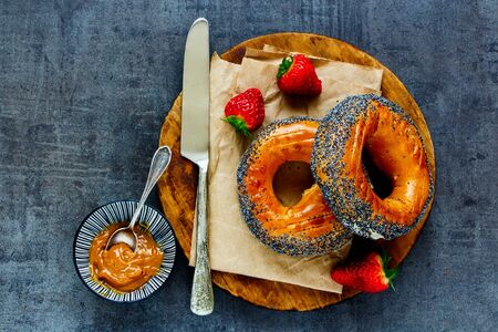 Breakfast set with whole grain bagels, strawberries and salted caramel spread on dark surfaceの写真素材