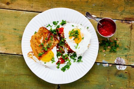 Fried eggs on grilled bread with fresh herbs over old wooden tableの写真素材