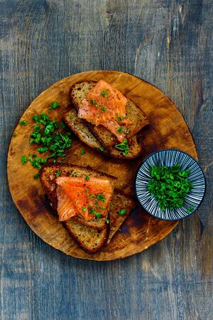 Tasty smoked salmon and herbs on grilled bread on wooden cutting boardの写真素材