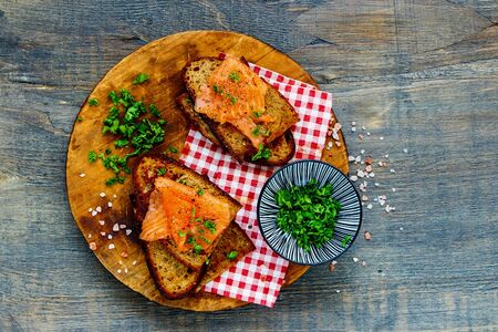 Fresh herbs with smoked salmon on grilled bread on wooden cutting boardの写真素材