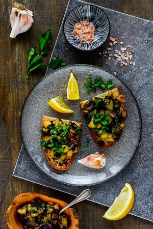 Oven-roasted warm aubergine salad with fresh herbs on bread flat-layの写真素材