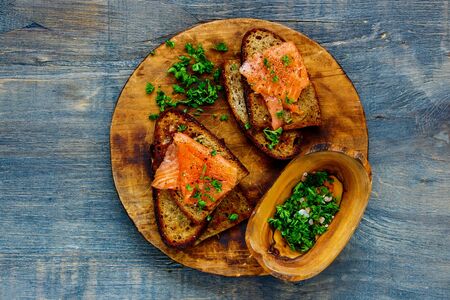Smoked salmon and fresh herbs on grilled bread on wooden cutting boardの写真素材