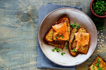 Smoked salmon and fresh herbs on grilled bread in plate flat layの写真素材