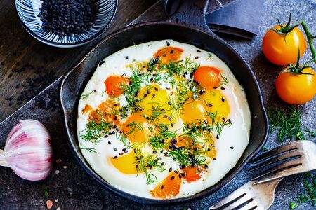 Fried eggs with fresh dill and tomato in a hot black pan close-upの写真素材