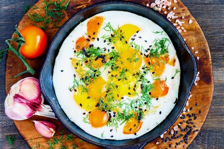 Fried eggs with fresh dill and tomato in a hot, black panの写真素材