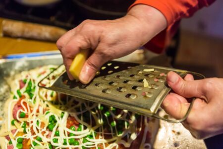 Preparing home pizza. Woman rubbing cheese on the kitchen, closeupの写真素材