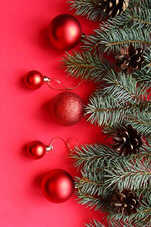 Christmas tree branches with red baubles on red background. Flat lay, top view, vertical, banner. Xmas greeting cardの写真素材