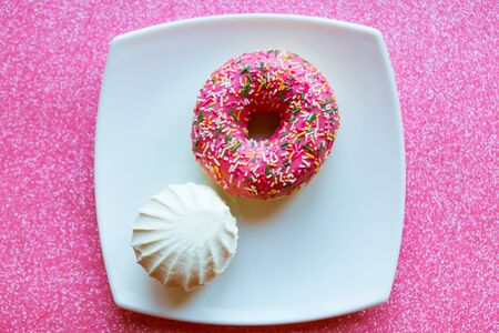 White vanilla zefir and pink donut on white plate, pink glitter background, top viewの写真素材