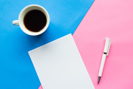 Flat lay photo with coffee cup and white paper blank on geometric blue and pink paper background