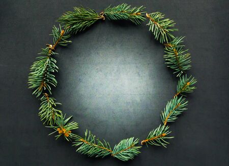 Christmas wreath of blue spruce branches on black background, top view. Flat lay photo, copy space for the textの写真素材