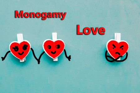 Three red wooden hearts on blue background and the text - monogamy loveの写真素材