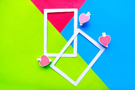 White photo frame on geometric green, blue and red paper background with hearts. Minimal concept. Valentine's Day greeting cardの写真素材