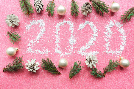 White numbers 2020 and christmas decorations  on pink glitter background. New Year concept