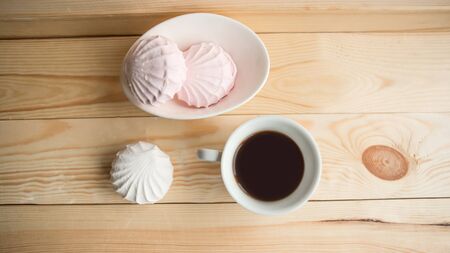 White zefir and coffee cup on wooden table, top view. の写真素材