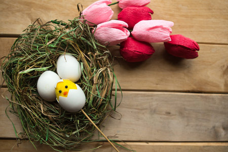 Flat lay photo with chicken eggs and toy chicken in straw nest and bouquet of tulips. Easter...