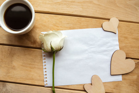 White rose, coffee cup and white mockup blank on wooden background. Valentine's Day or Wedding...