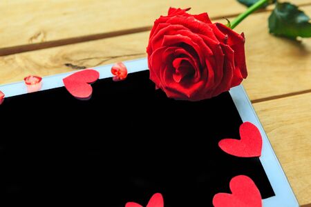 Red rose and decorative hearts on the mockup tablet. Valentine's Day, Wedding or Mother's Day greeting card. Copy space for the textの写真素材