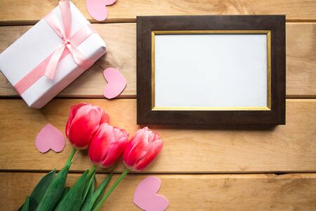 Pink tulips, mockup photo frame and gift box on wooden background. Flat lay, top view, copy space. Women's Day or Mother's Day greeting cardの写真素材