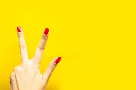 Woman's hand shows the victory gesture over bright yellow background. Minimal concept. Copy space...