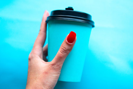 Womanâs hand holds take away coffee cup over blue background. Copy space for the textの写真素材