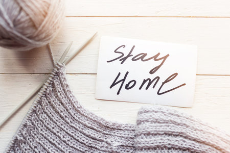 Knitting, ball of gray thread and card with message Stay Home on wooden background.