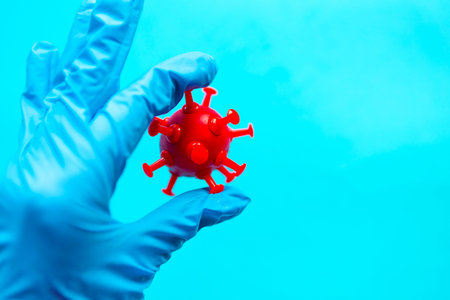 Hand in blue medical glove holds red coronavirus. Covid-19 concept