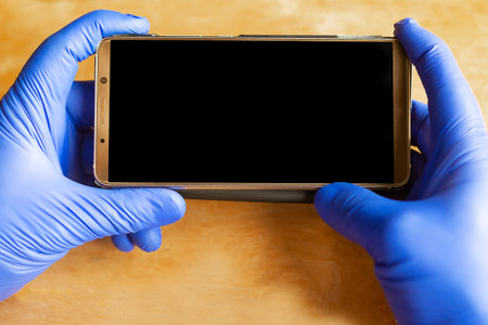 Hands in medical gloves holds mobile phone over wooden background