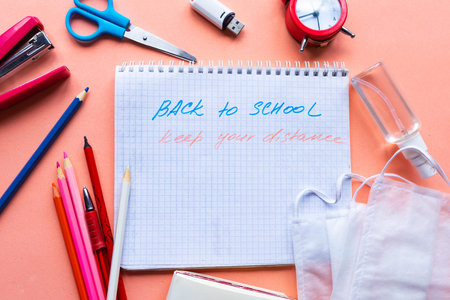 School supplies, notebook with the text Back to School and medical mask on pink backgrpund. Back to...