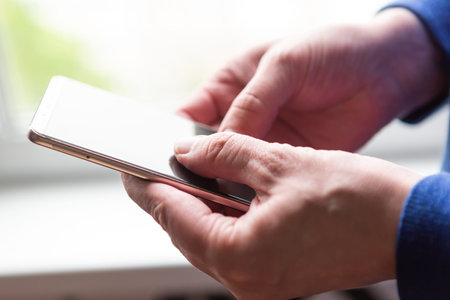 Close up of a man using mobile smart phone near the window