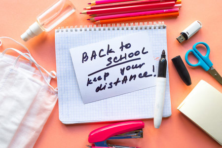 School supplies, medical mask and card with message Back to School â€“ Keep your distance. ...