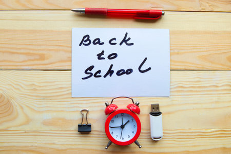 Alarm clock, pen and card with message Back to School on wooden table
