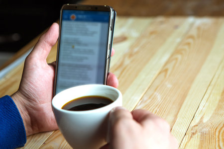 Manâ€™s hands with a phone and coffee cup, closeup