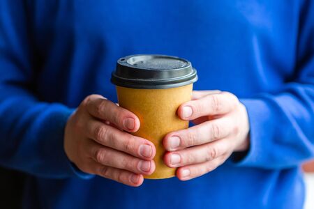Man in blue sweater holds a coffee cup in his handsの写真素材