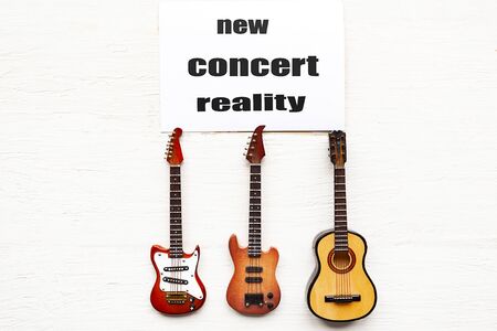 Acoustic guitar, electric guitar, bass guitar and card with message New Concert Reality on wooden background.  Concert quarantine conceptの写真素材