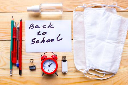 School supplies, medical mask and card with message Back to School on wooden background. School quarantine conceptの写真素材