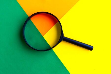 Magnifying glass on geometric green, orange and yellow background. Minimal conceptの写真素材
