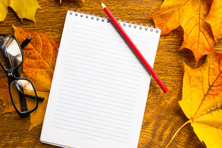 White mockup notebook and coffee cup on autumn foliage background, top view