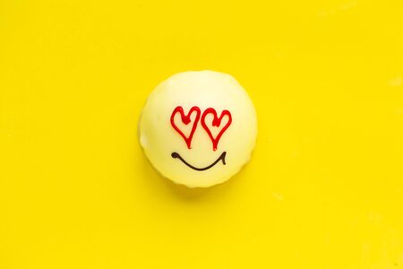 Tasty sweet cake with draw face and heart eyes on bright yellow background, top view. Love concept.の写真素材