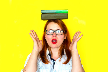 Redhead girl in white blouse and glasses with books on yellow background.