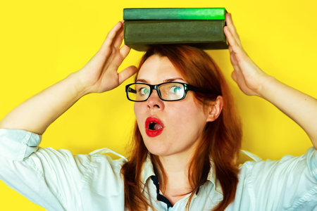 Redhead girl in white blouse and glasses with books on yellow background.
