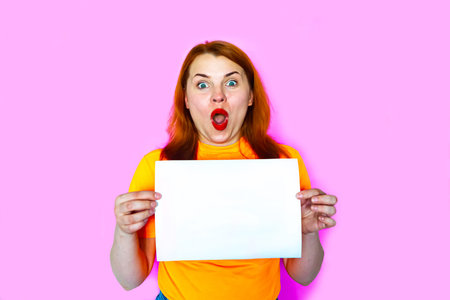 Redhead girl is holding white mockup blank on pink background