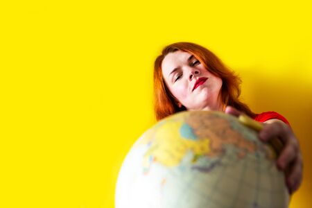 Portrait of beautiful redhead girl with globe on yellow background, travel conceptの写真素材