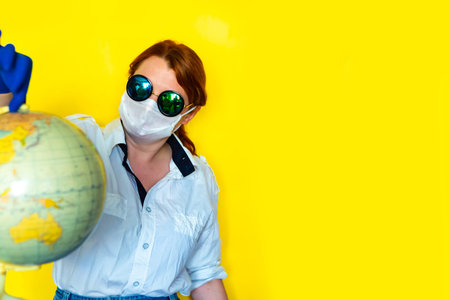 Girl in medical mask and sunglasses is looking for a place on the map to travel.の写真素材