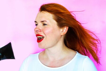 Portrait of a girl with hairdryer on pink background, copy spaceの写真素材